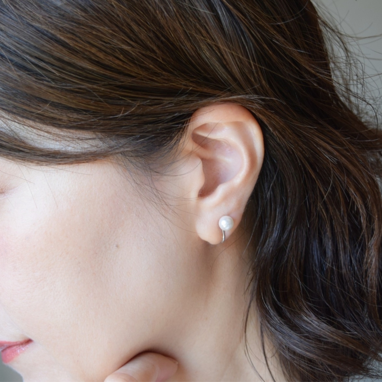 大人の女性の耳元に着用された、6mmの一粒パールイヤリング。シルバーの上品な艶とパールの輝きがお顔周りをパッと華やかにライトアップし、ピアスのように華奢に馴染んでいる様子。