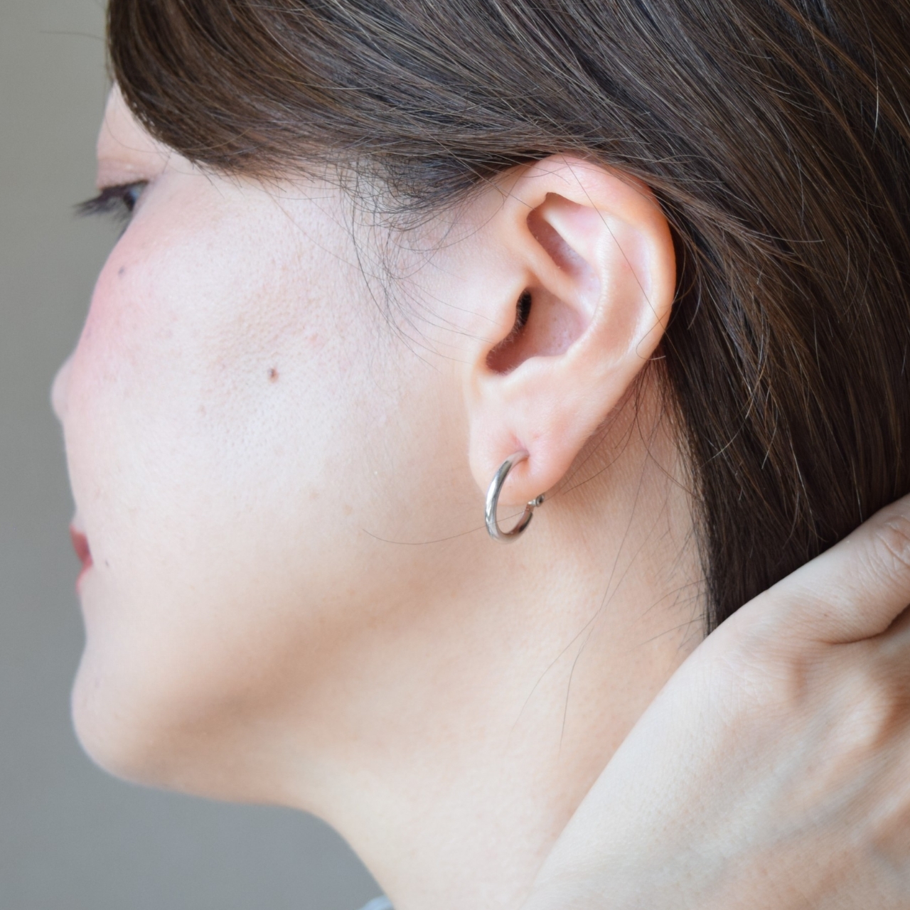 大人の女性の耳元に着用された、シルバー925製のフープイヤリング。洗練されたシルバーのフープラインが横顔をすっきりとした印象に仕上げ、華奢に馴染んでいる様子。
