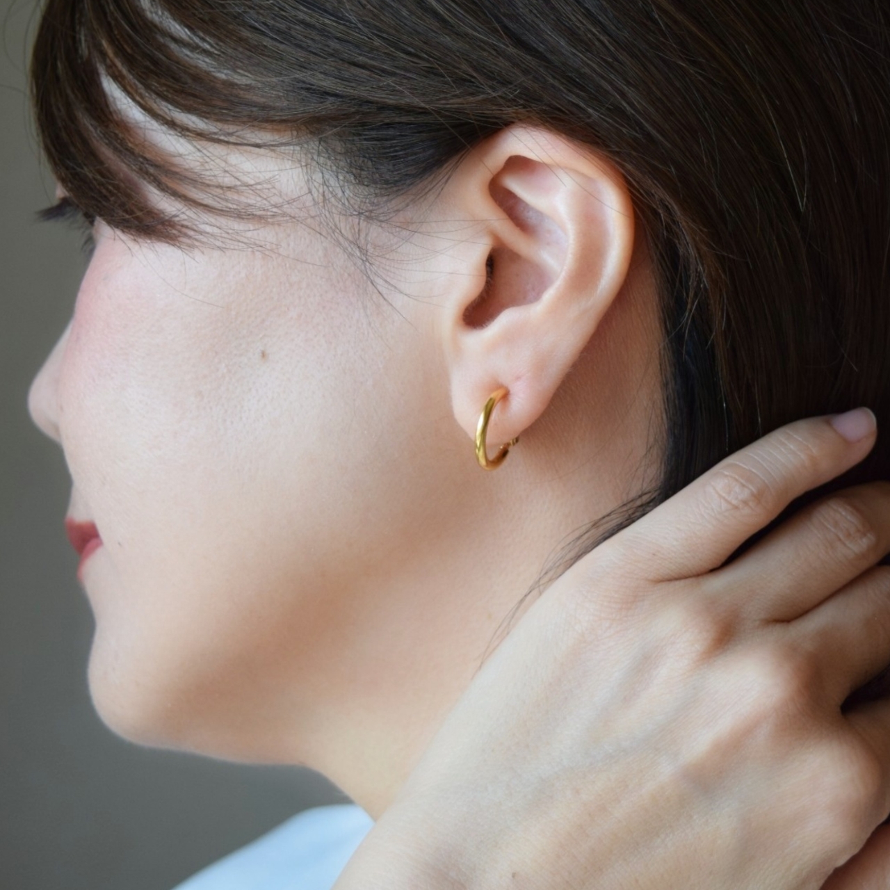 大人の女性の耳元に着用された、24金GPゴールドのフープイヤリング。洗練されたゴールドフープラインが横顔をすっきりとした印象に仕上げ、華奢に馴染んでいる様子。