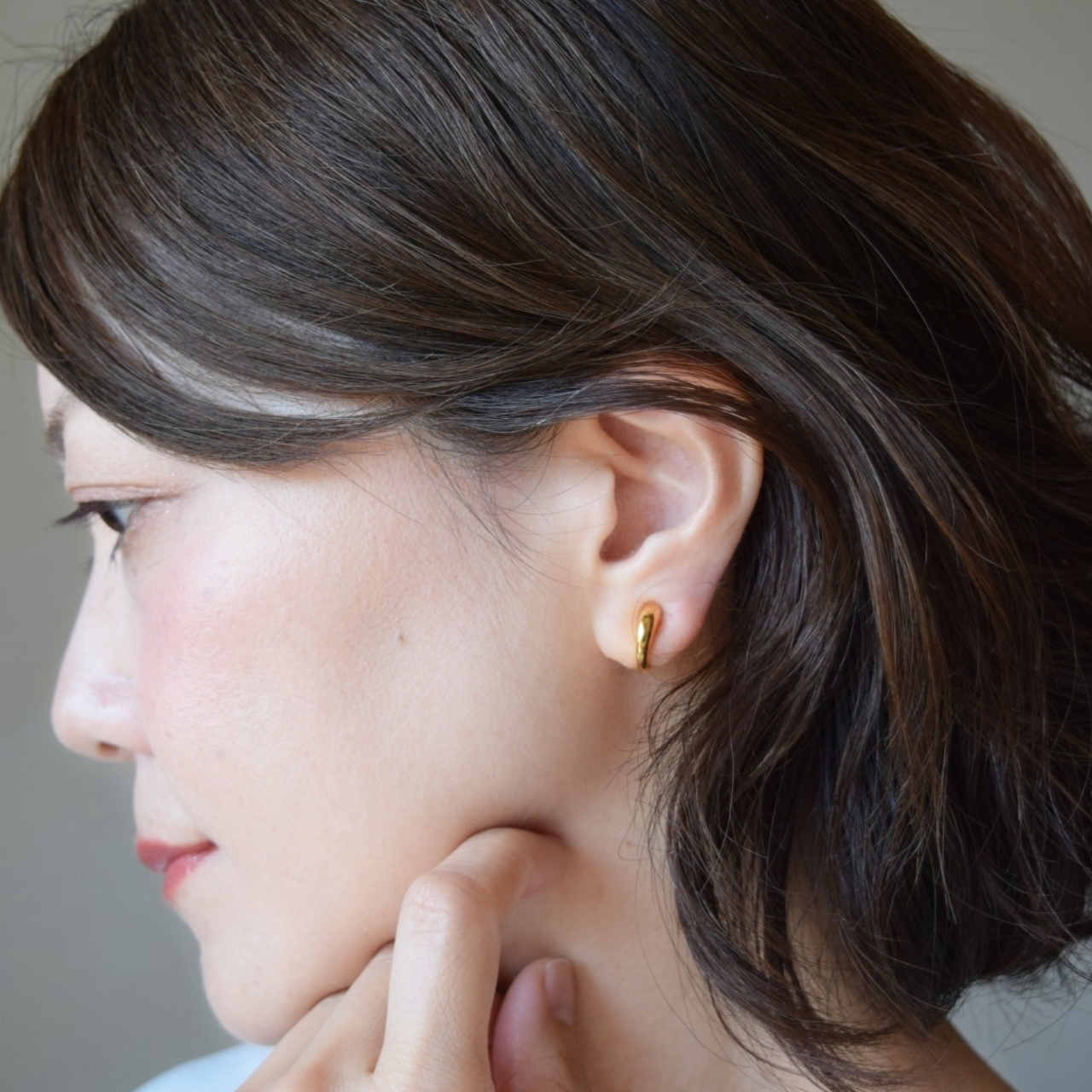 大人の女性の耳元に着用された、24金純金コーティングの地金イヤリング。無駄のないシルエットとゴールドの華やかさがモダンな印象を添え、ピアスのように軽やかに馴染んでいる様子。