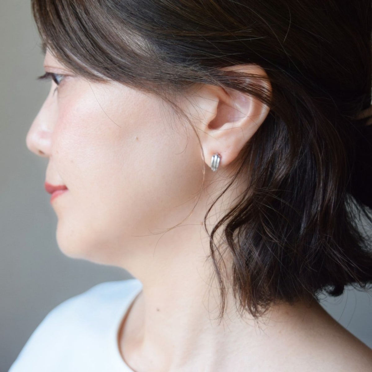 大人の女性の耳元に着用された、シルバー925製の縦ラインイヤリング。立体感のあるスタイリッシュなシルエットが耳元を品よく引き締め、ピアスのように華奢に馴染んでいる様子。