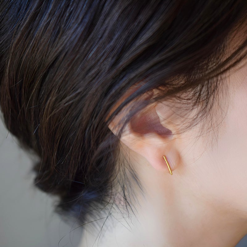 女性の耳元の着用カット。ブルーサファイアのチャームを取り外し、縦のラインが美しい極シンプルなゴールドのミニフープ（バー）パーツだけで着用した、上品でミニマルなスタイリングを表現しています。